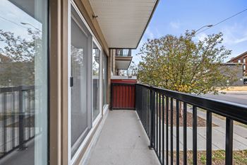 A balcony with a black railing and a view of a tree and a building.